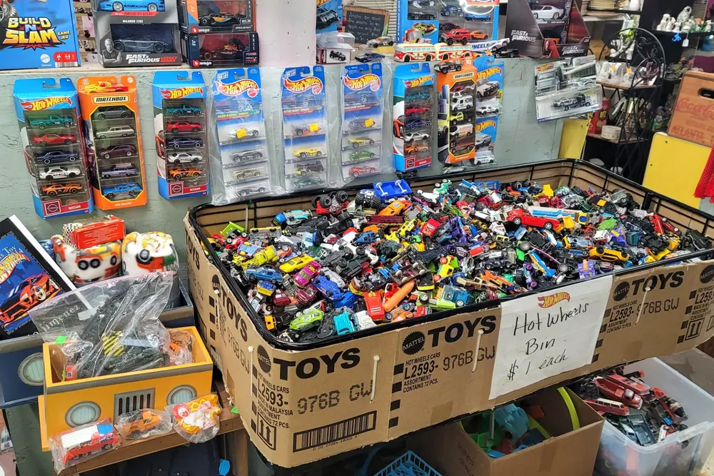 A cardboard bin full of loose Hot Wheels cars marked one dollar each, with carded multi-packs on the wall above