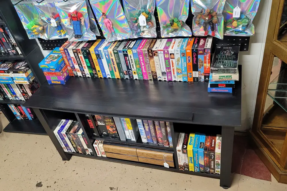 Shelves of VHS tapes under a row of bagged vintage action figures